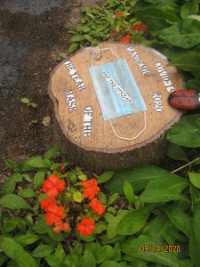 A piece of garden art using a stump, flowers, and a medical mask